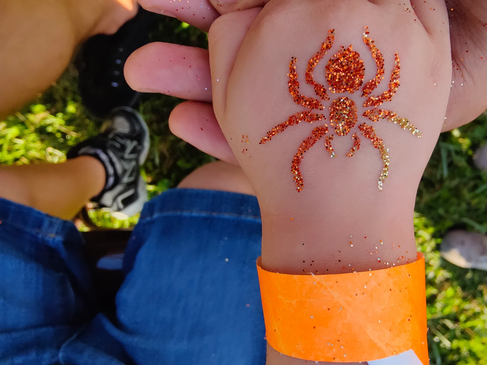 Orange glitter spider design on the back of a hand